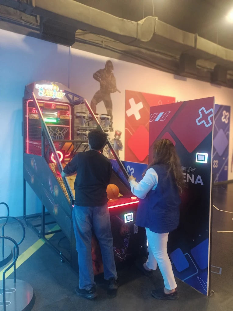 Two people play a basketball arcade game in an entertainment venue.