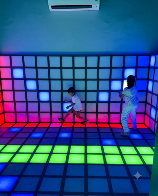 Two children play on a light-up dance floor in a room with illuminated walls.