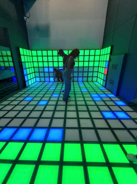 A young woman dances on a light-up floor in a room with a grid of green and blue lights.