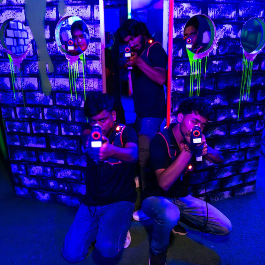 Young men play laser tag in a dimly lit, neon-lit arena, aiming their glowing phasers.