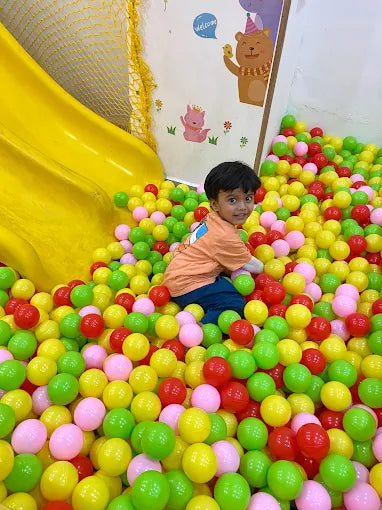 Child playing in a pit of colorful balls with a yellow slide in the background