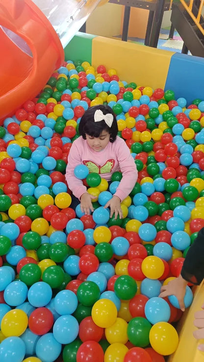 Child playing in a colorful ball pit with various colored balls.
