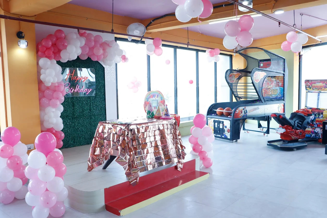 Decorated room with balloons, a table, and arcade machine.