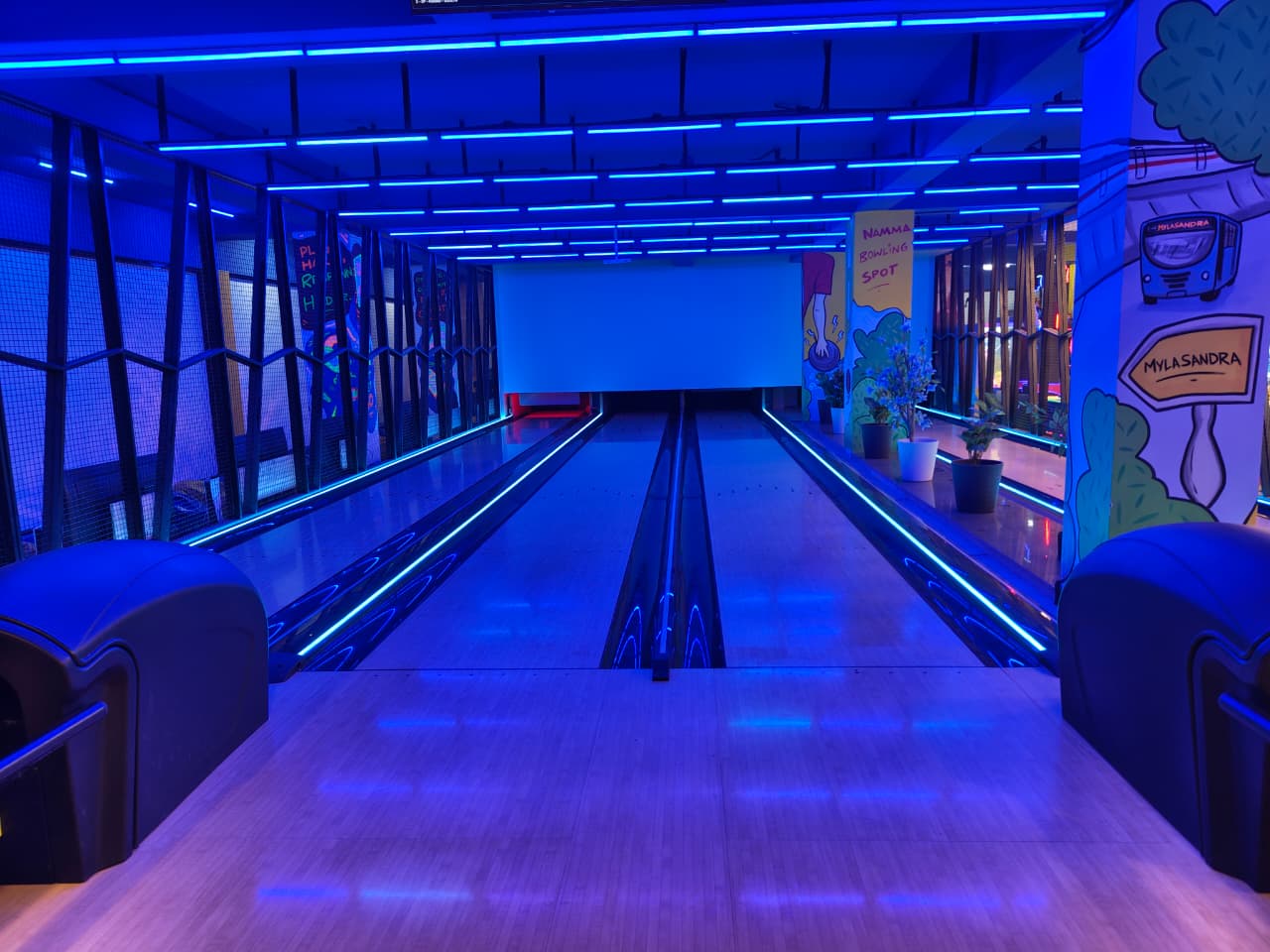 A bowling alley with neon blue lights and colorful murals.