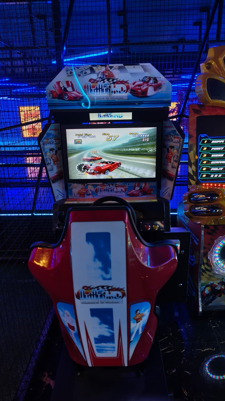 A racing arcade game with a red car on screen, set in an arcade with blue lighting.