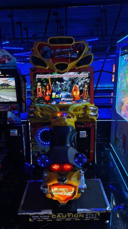 An arcade motorcycle game with a screen showing a racing game and two women holding trophies.