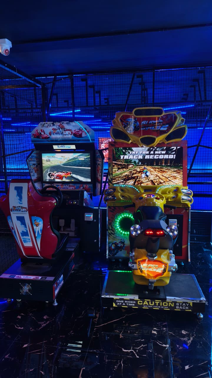 Arcade racing games with a motorcycle theme, set in a dimly lit arcade with blue neon lights.