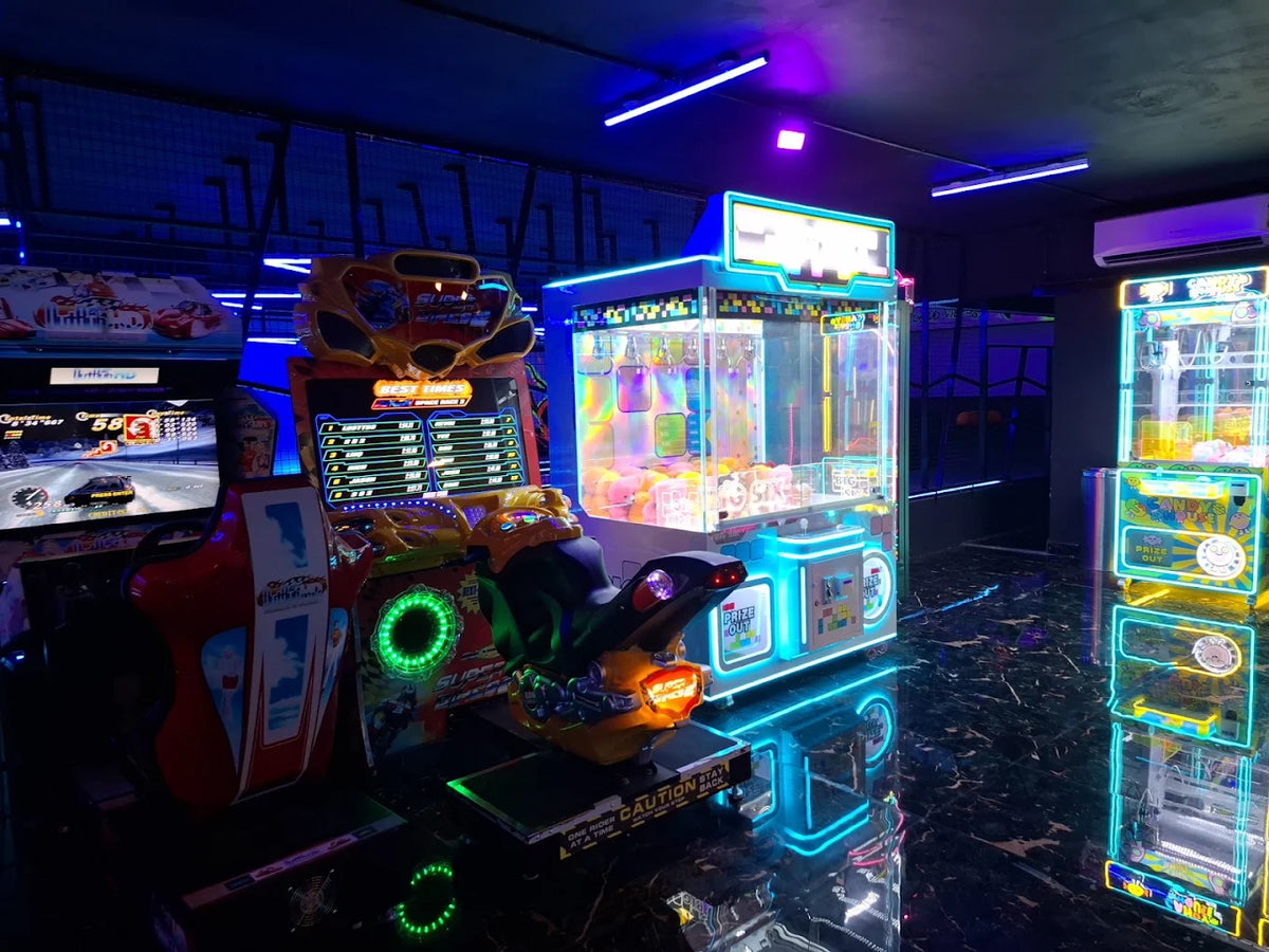 Arcade with neon-lit games, including racing simulators and claw machines, reflecting on a dark, glossy floor.