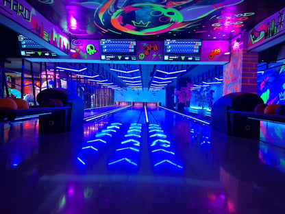A neon-lit bowling alley with glowing blue lanes and vibrant graffiti art on the ceiling.