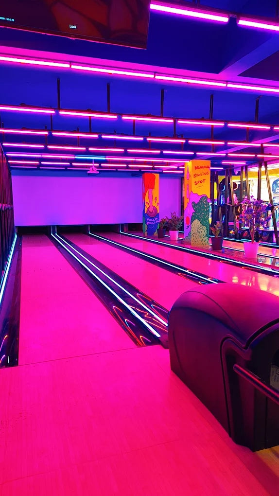 A neon-lit bowling alley with pink and blue lights, featuring bowling lanes and colorful murals.