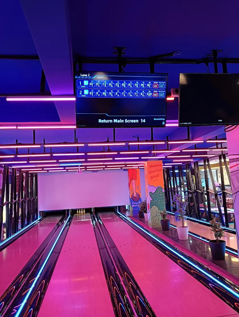 A bowling alley with neon lights and a digital scoreboard showing game scores.