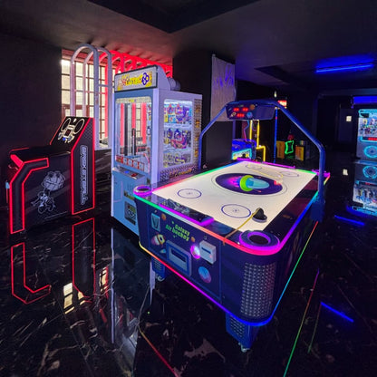 An arcade with air hockey and claw machines, lit by neon lights.