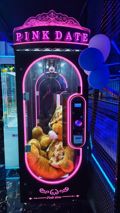 A claw machine with "PINK DATE" lit up in neon, filled with plush toys, and a person reflected in the glass.