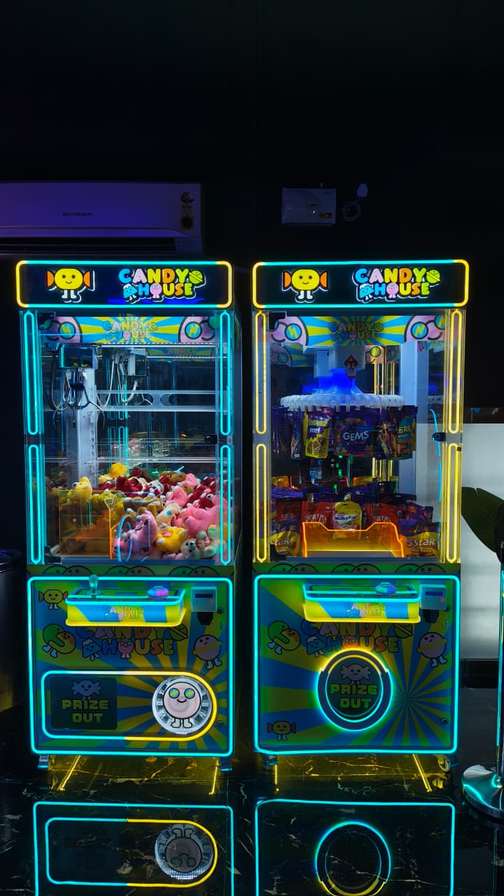 Two brightly lit arcade claw machines, one filled with plush toys and the other with candy, stand side-by-side in a dark arcade.