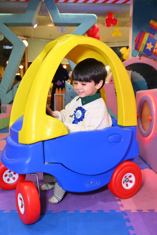 A young boy in a toy car at a birthday party.