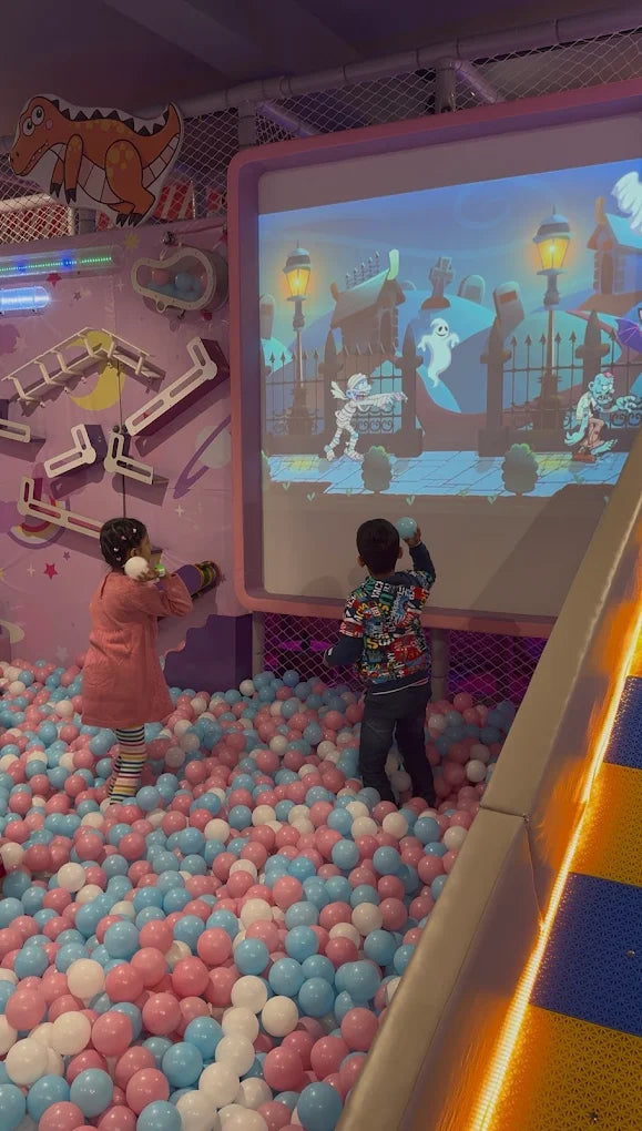 Children play in a ball pit in front of a projected Halloween-themed game.