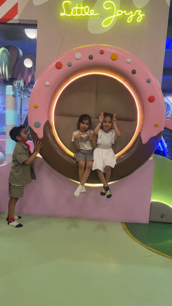 Two young girls sit in a donut-shaped seat while a young boy stands nearby.