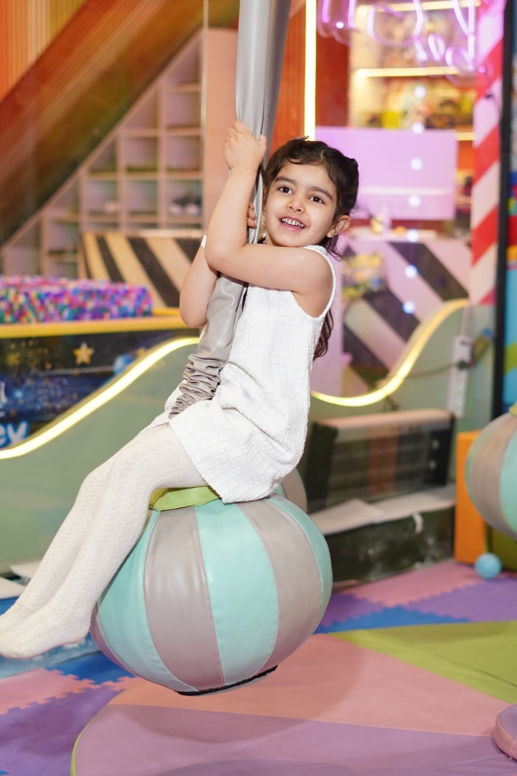 A young girl on a swing in a colorful indoor play area.