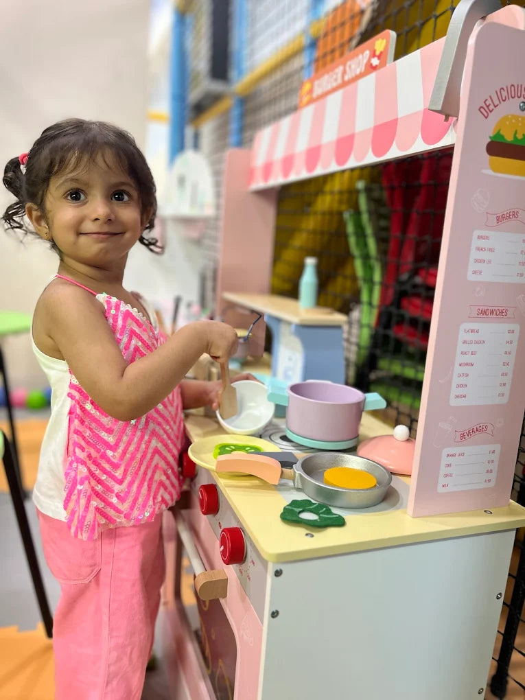 A young girl plays with a toy kitchen in a brightly colored play area.