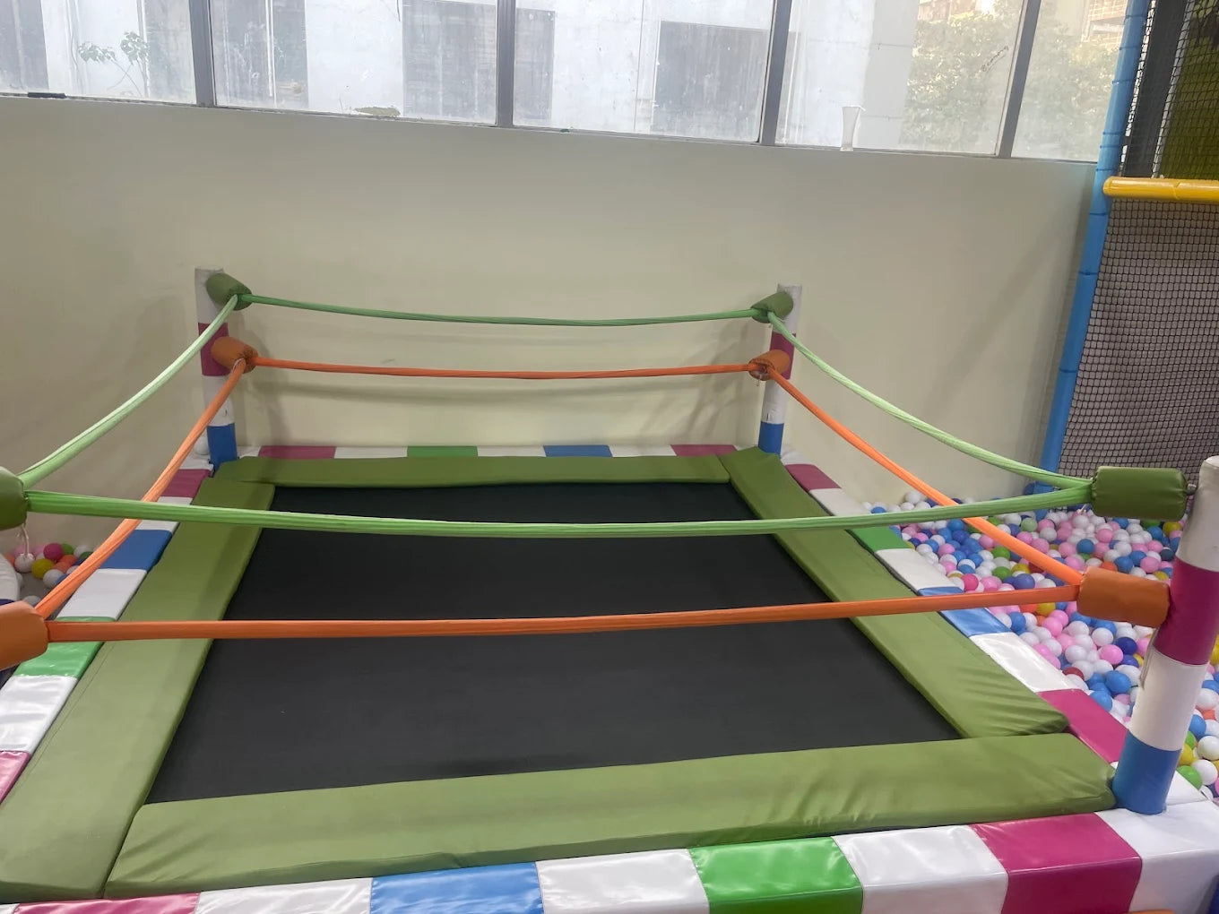 A colorful indoor play area with a trampoline surrounded by a ball pit and soft padding.