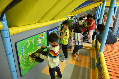 Children play with interactive musical panels in a colorful indoor playground.