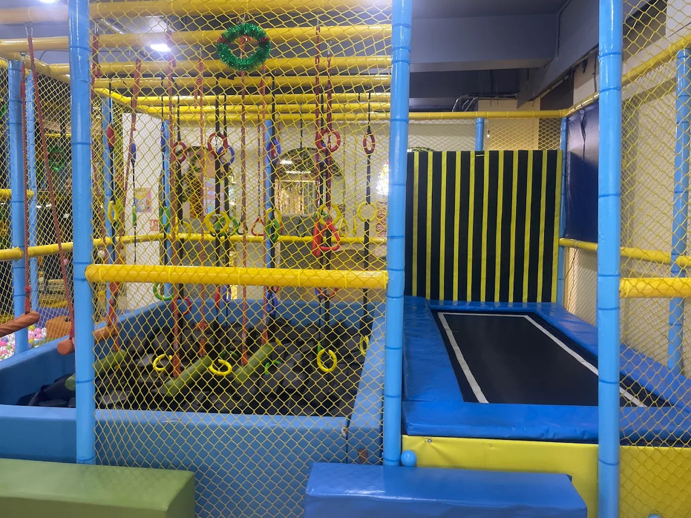 A colorful indoor playground with a trampoline, rings, and a ball pit for children.
