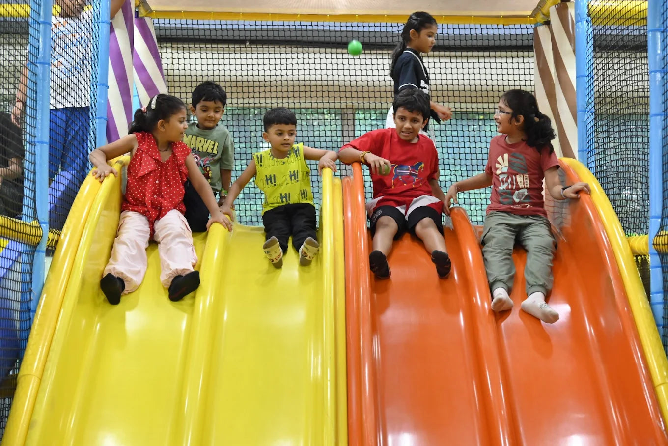 Children slide down colorful playground slides at an indoor play area.
