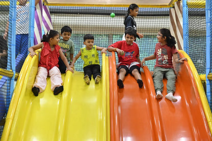 Children slide down colorful playground slides at an indoor play area.