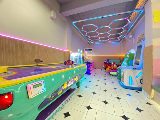 An arcade with air hockey, video games, and a claw machine, illuminated by colorful LED lights.