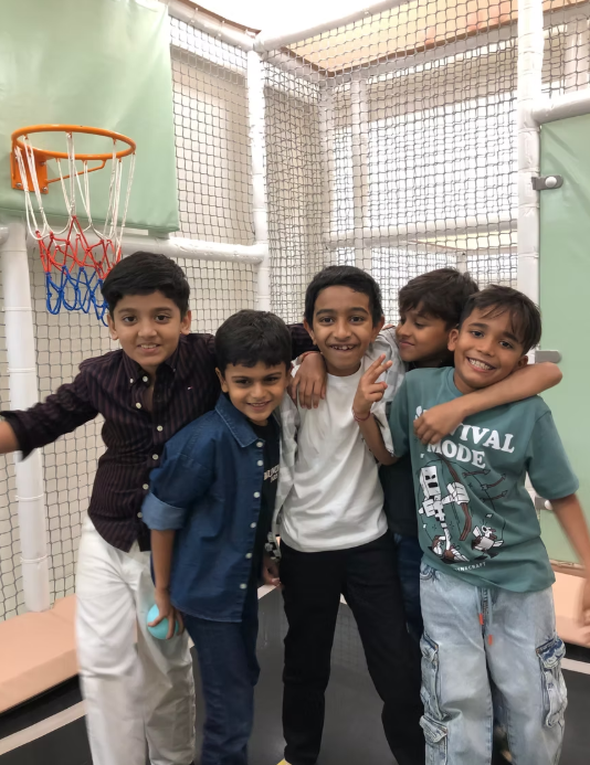 Five young boys pose for a photo in a play area with a basketball hoop.