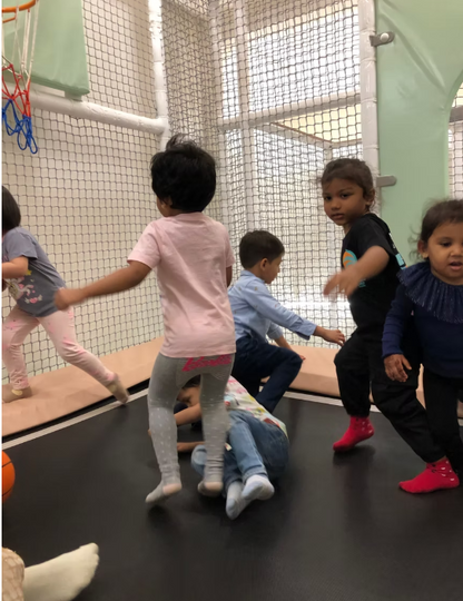Young children play on a trampoline in an indoor play area.