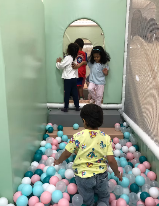 Children play in a ball pit and on a slide in an indoor playground.