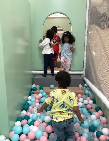 Children play in a ball pit and on a slide in an indoor playground.