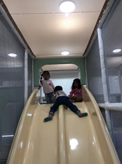 Three young children play on a plastic slide in an indoor play area.