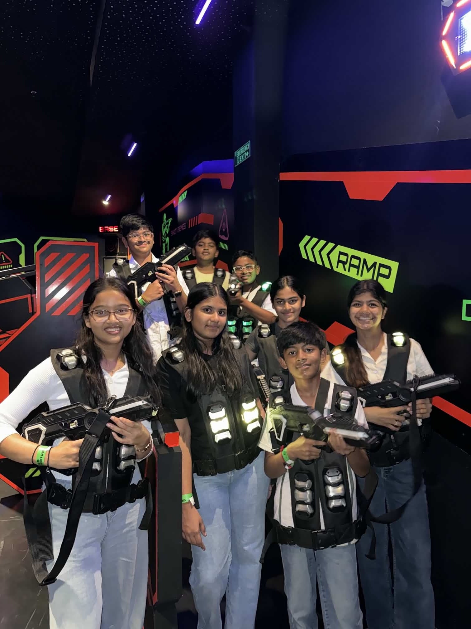A group of young people in laser tag vests and holding phasers smile at the camera in a dimly lit arena.