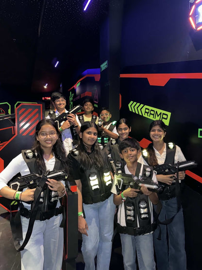 A group of young people in laser tag vests and holding phasers smile at the camera in a dimly lit arena.