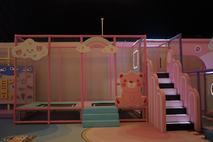 A brightly colored indoor playground with a trampoline, slide, and climbing wall for children.