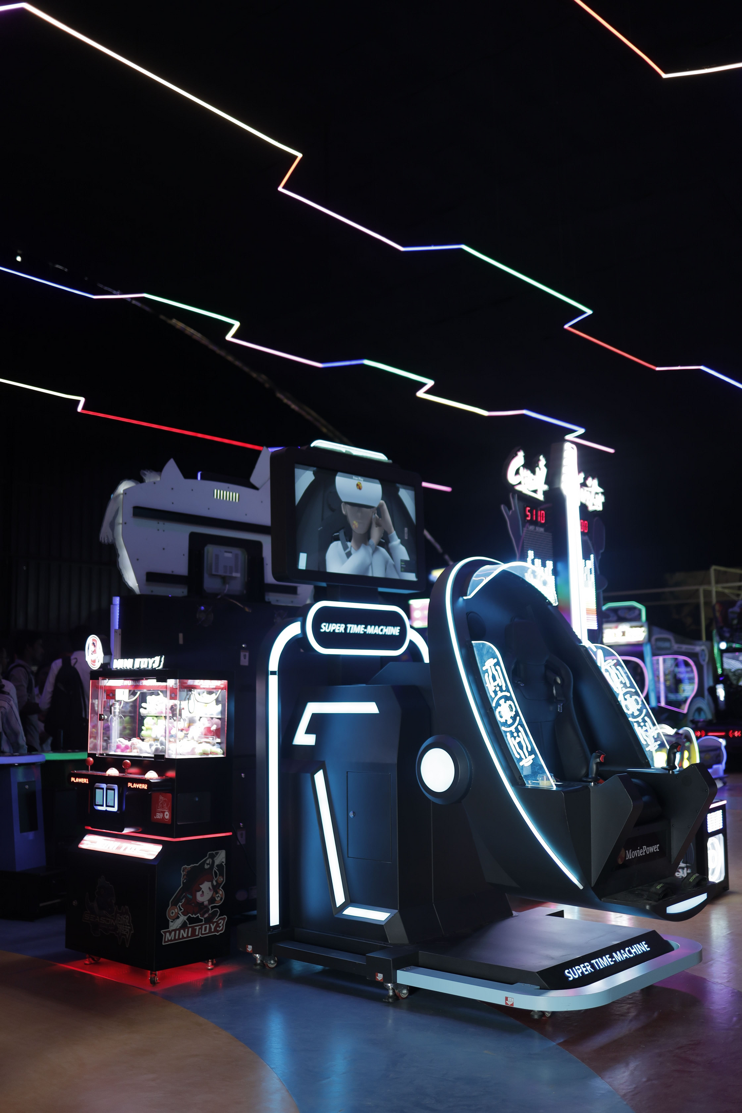 A VR simulator ride with neon lights and a claw machine in an arcade.