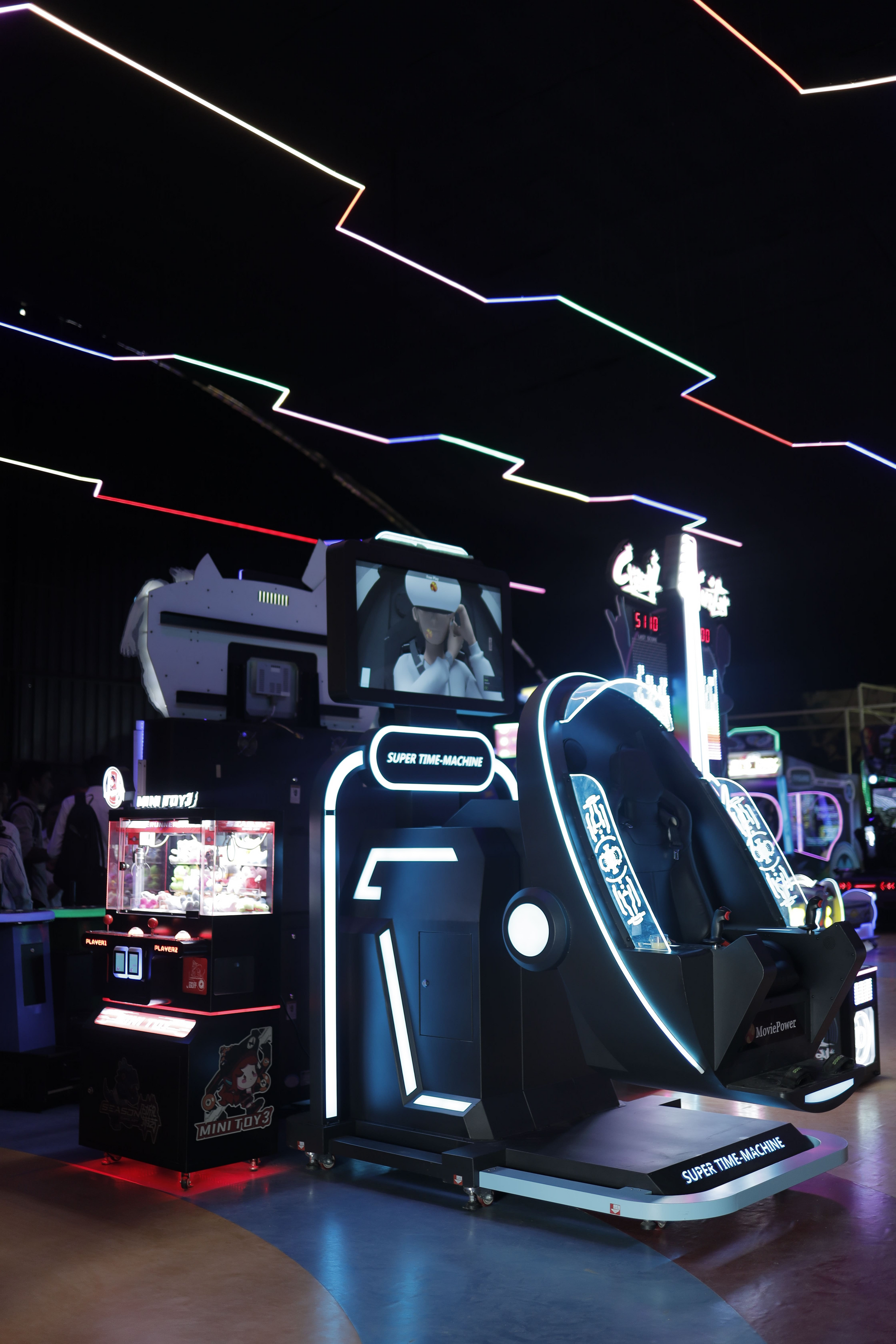 A VR simulator ride with neon lights and a claw machine in an arcade.