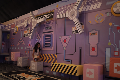 A young girl sits on a cube in a purple, sci-fi themed play area with colorful blocks.