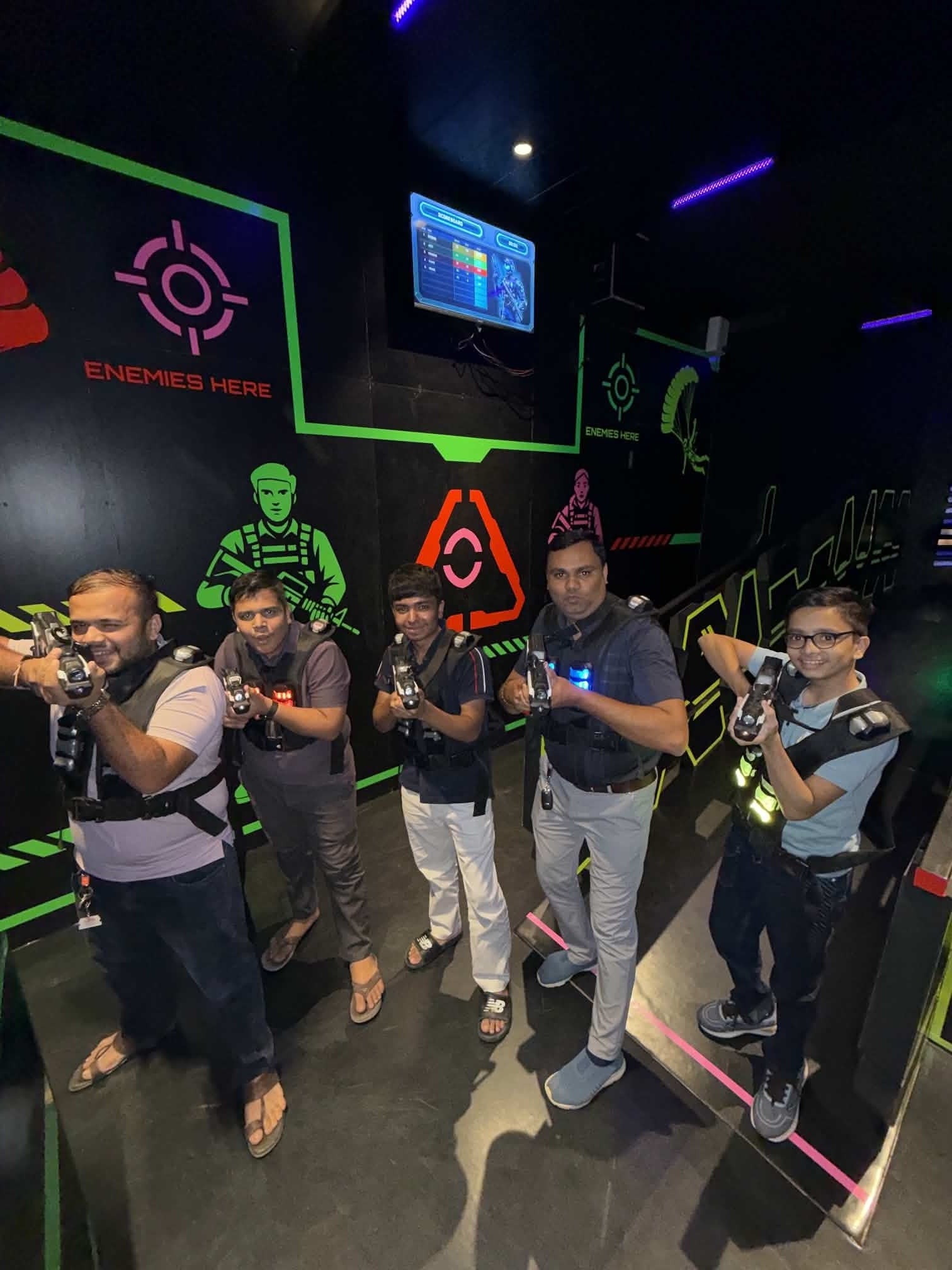 Adults and a child play laser tag in a dark arena with neon lights and graphics.