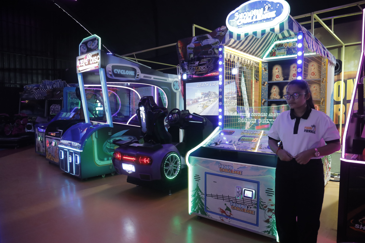 A young woman stands in an arcade next to several colorful racing and carnival games.