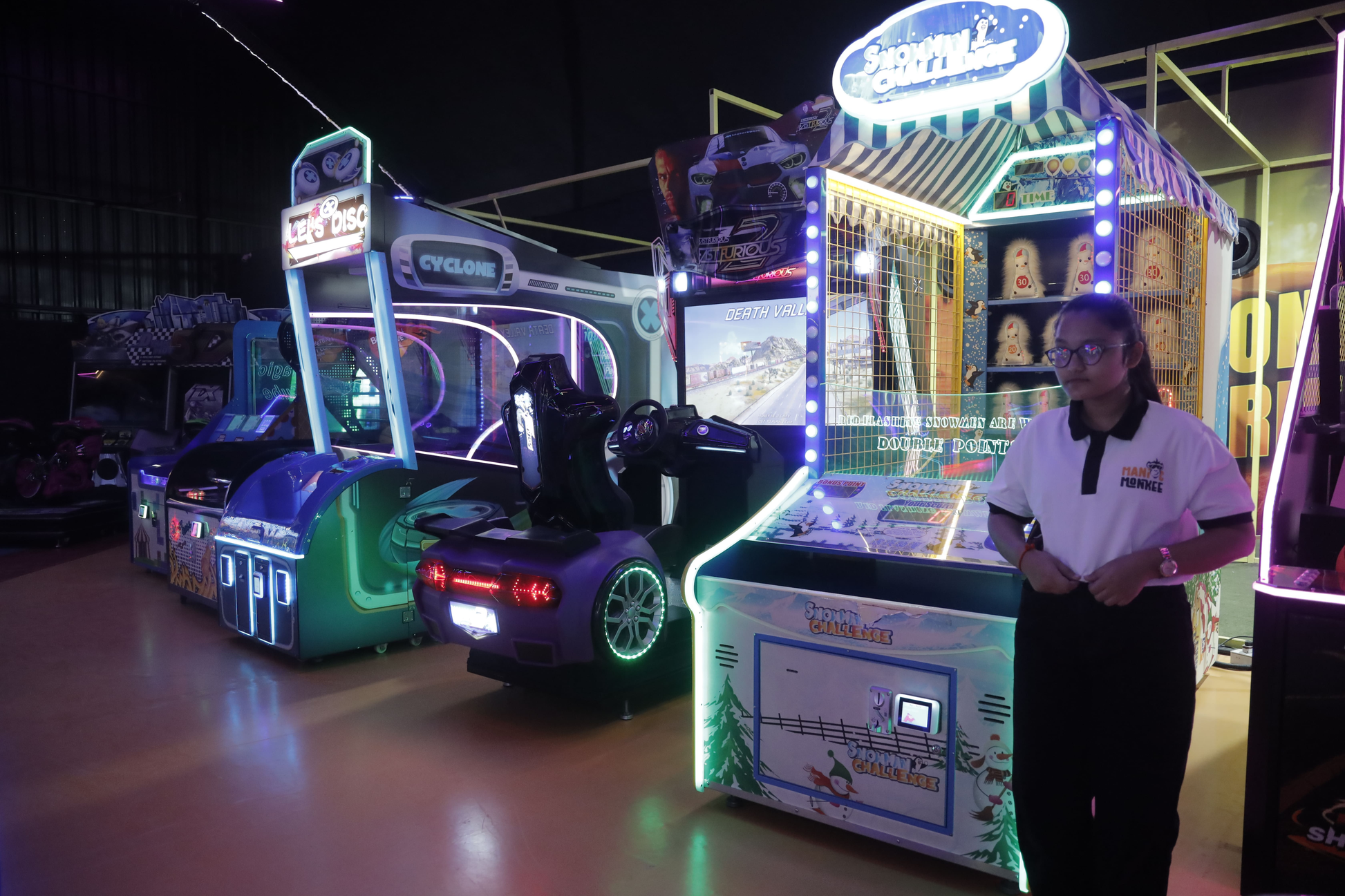 A young woman stands in an arcade next to several colorful racing and carnival games.