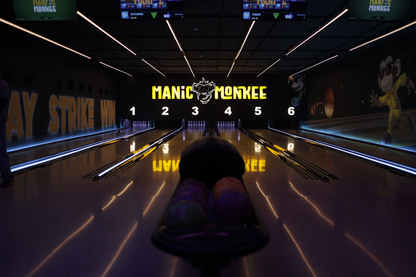 A bowling alley with illuminated lanes and pins, featuring a "Manic Monkee" logo.