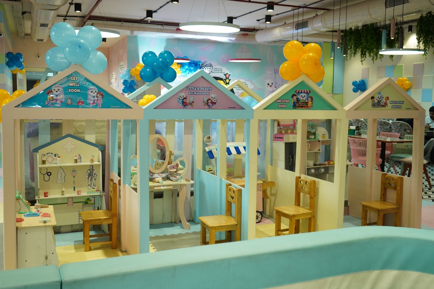 Playhouses for children, including a doctor's office, salon, and shop, are decorated with balloons.