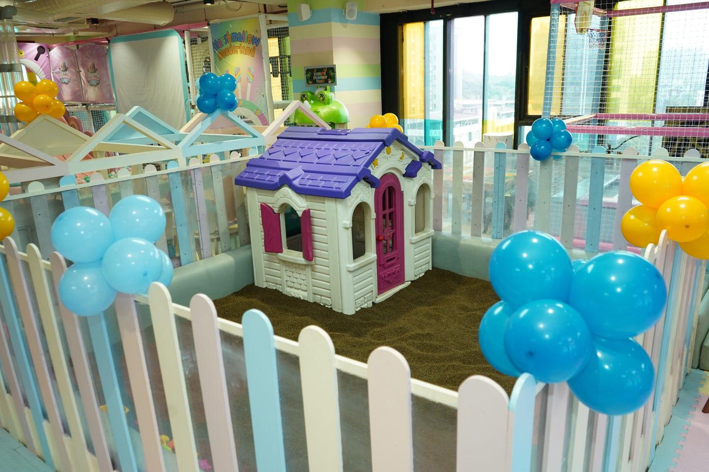 A colorful indoor playground with a playhouse, balloons, and a ball pit for children.