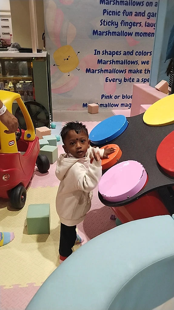 A young child stands in a colorful play area with a toy car and a large interactive game.