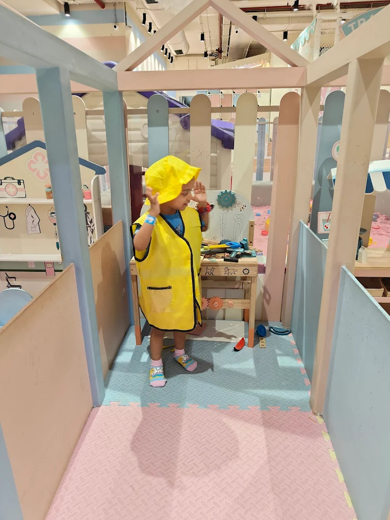 A young child in a yellow hat and vest plays in a colorful indoor play area.