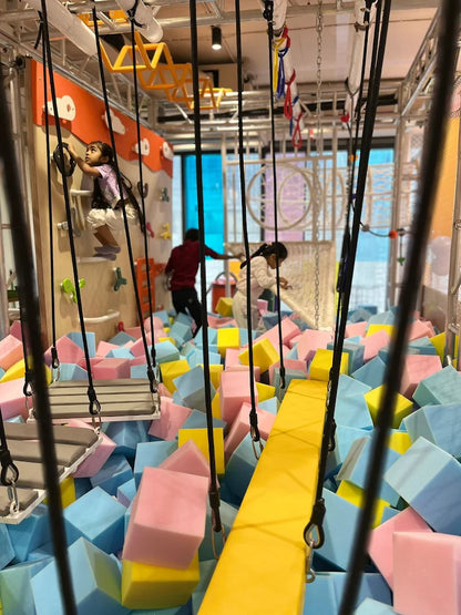 Children play in a colorful foam pit with climbing walls and swings.