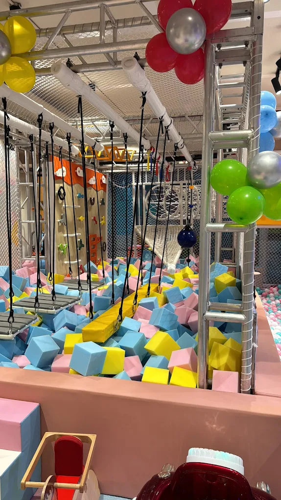 A colorful indoor playground with a foam pit, climbing wall, and obstacle course for children.